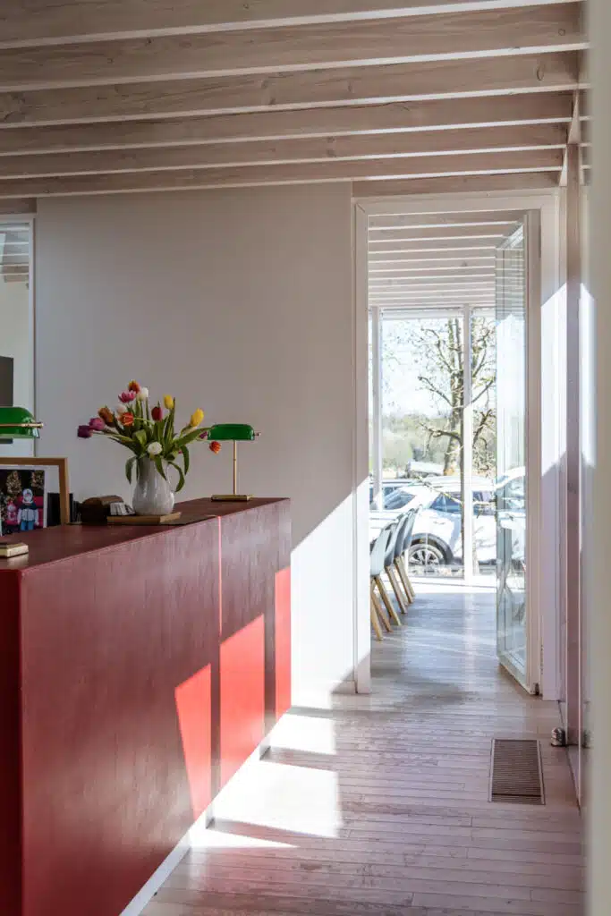 Modern notariskantoor interieur met houten balken, roze receptiebalie met tulpen en glazen deur naar buiten