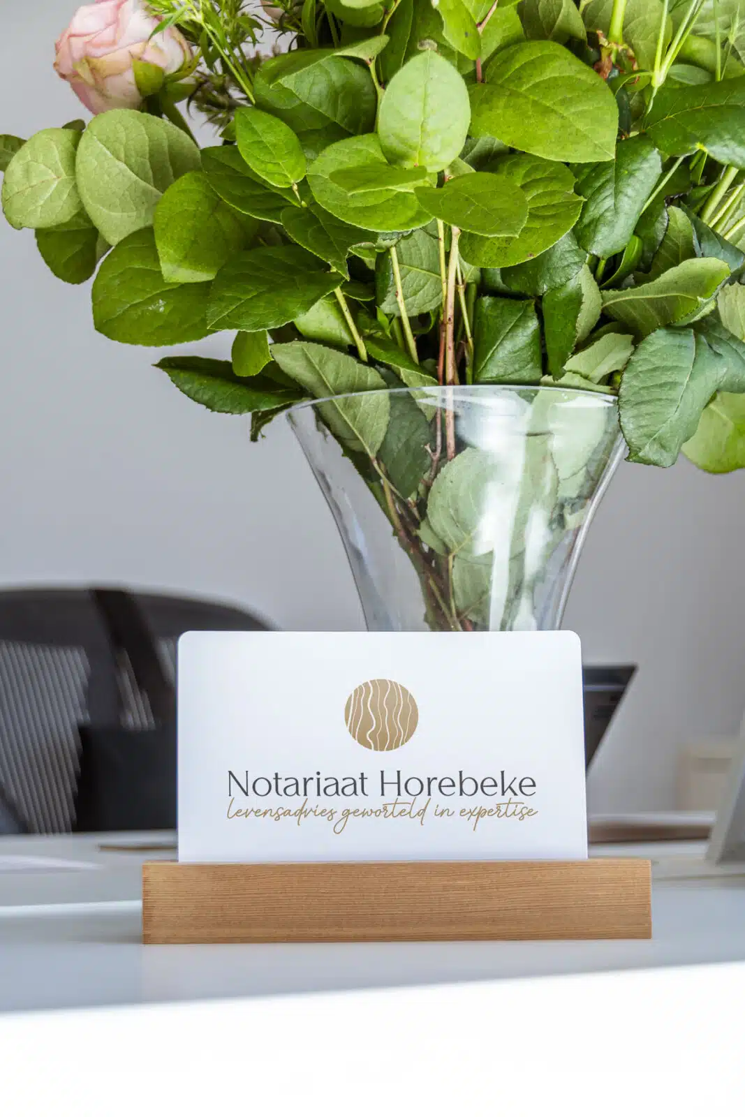 Notariaat Horebeke visitekaartje op houten standaard met rozen en groene bladeren op kantoorbureau