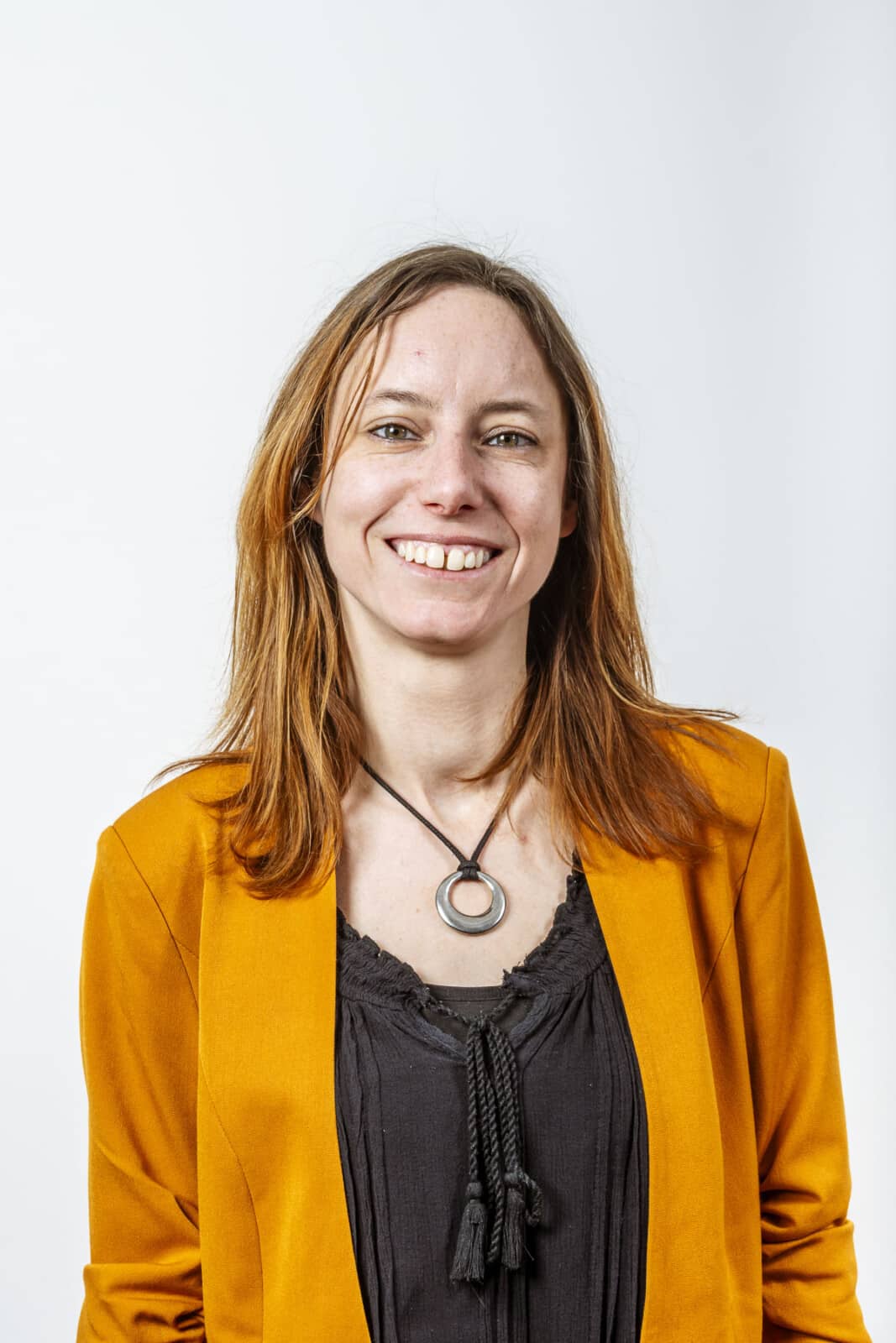 Professionele headshot van Sarah Goethals, teamlid van Notariaat Horebeke, glimlachend in geel jasje