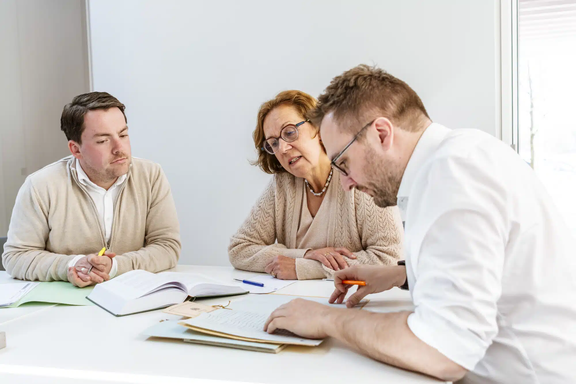 Drie professionals bespreken zakelijke documenten aan tafel tijdens adviesgesprek bij notariskantoor