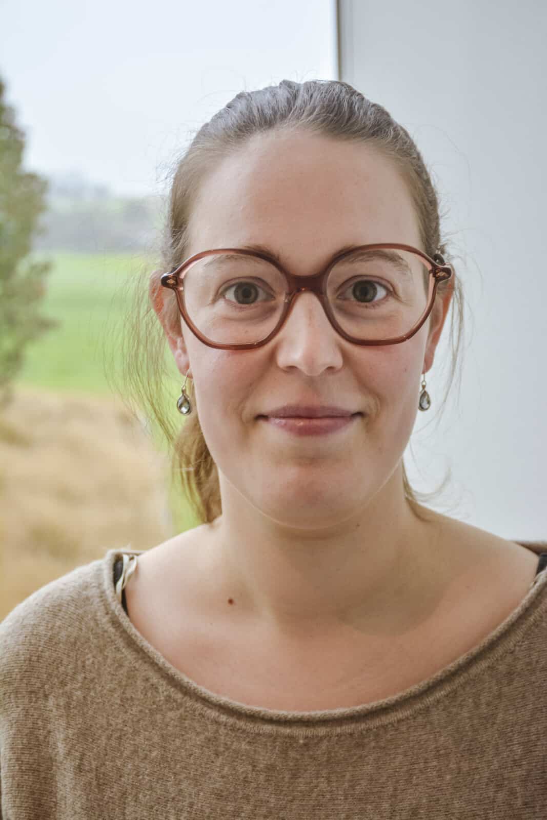 Camille Demeester, secretariaat medewerker van Notariaat Horebeke, glimlacht vriendelijk met bril en bruine trui