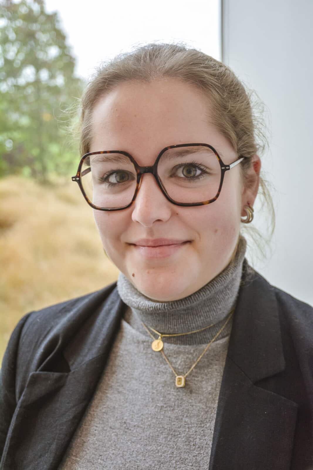 Caro Willems, notarieel medewerker bij Notariaat Horebeke, lacht vriendelijk met bril en grijze trui