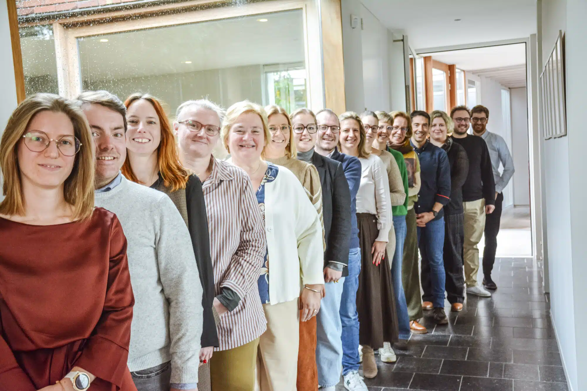 Het volledige team van Notariaat Horebeke staat in een rij in de moderne kantoorgang